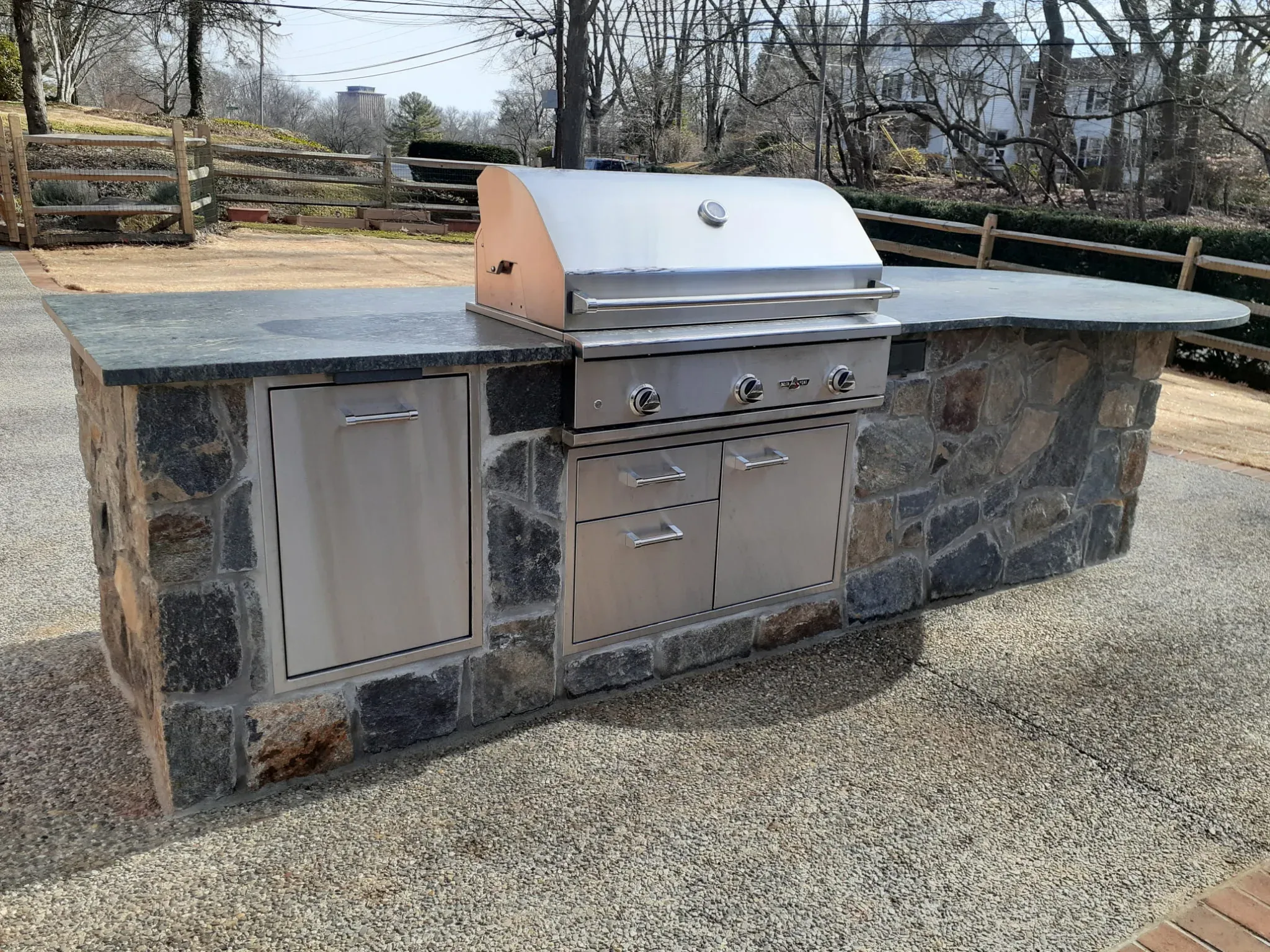 Custom-built outdoor kitchen with natural stone island, granite countertop and built-in stainless steel grill — high-end outdoor living by Zavala & Sons